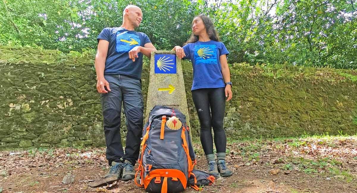 Campbell & Alya wearing Camino T-shirts at a distance pole marking the Camino de Santiago in Galicia