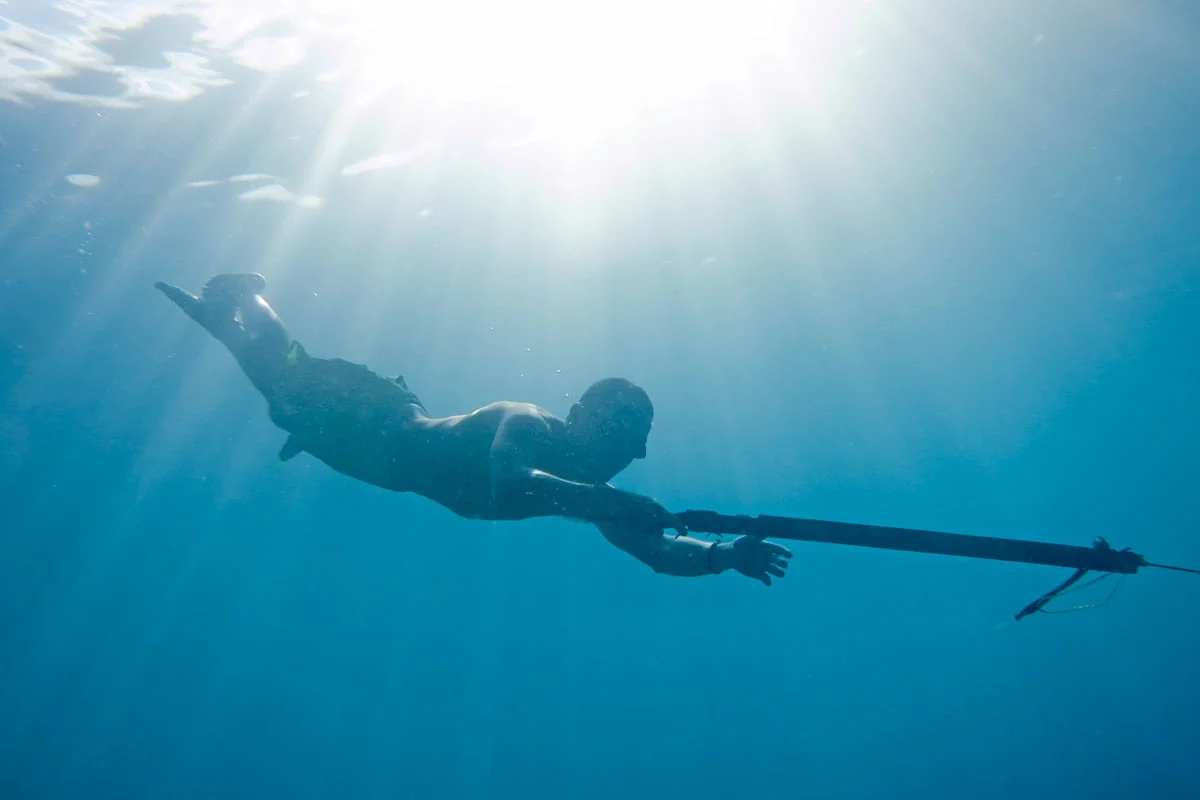 man diving barefoot with handmade speargun and wooden goggles