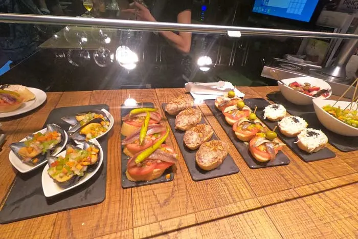 Different seafood and cold meat pintxos (small sandwiches) displayed at a bar