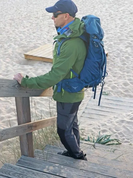 hiker with blue backpack standing next to the beach