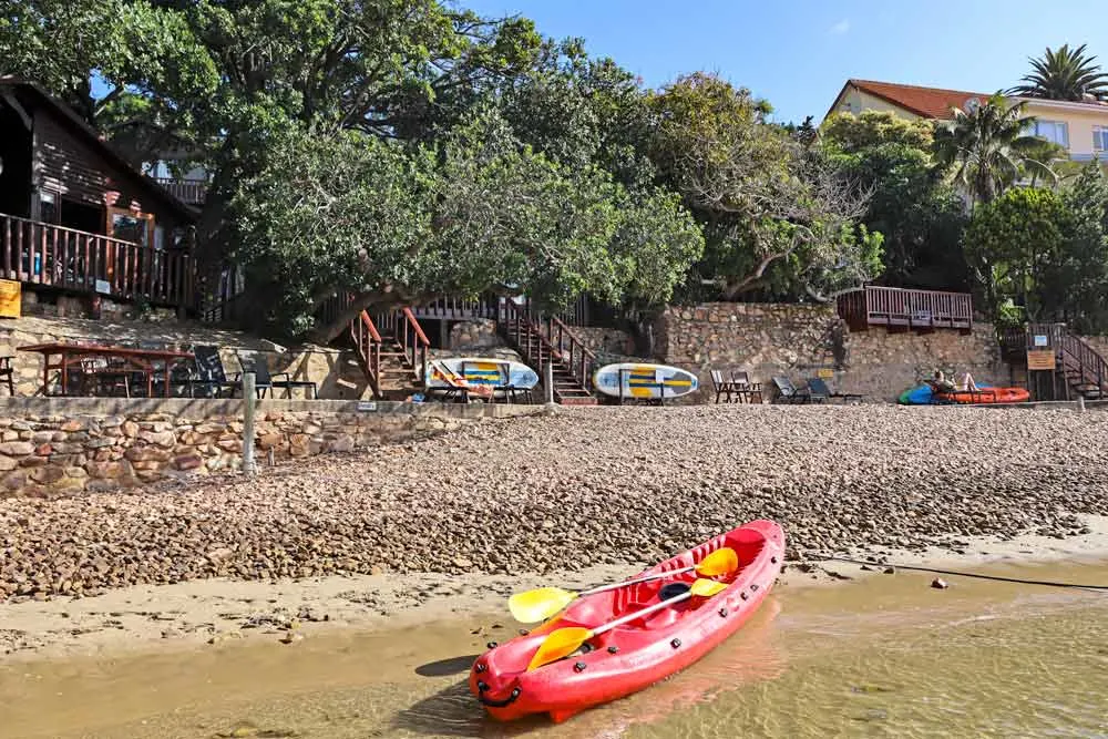 A sandy beach with kayaks surrounded by the forest in Knysna