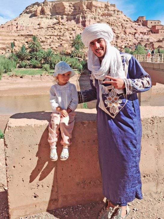 child and Berber man with village on hilltop in background