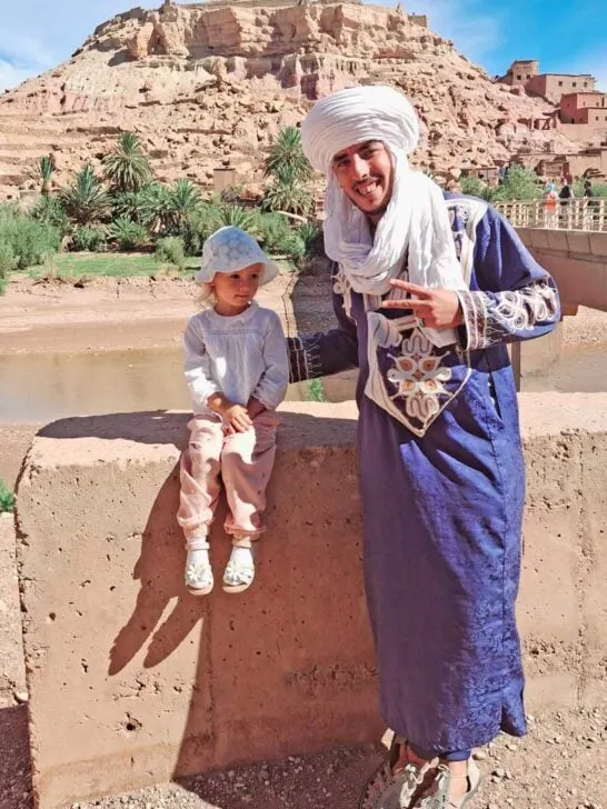 child and Berber man with village on hilltop in background