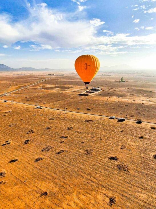 orange hot air balloon flying over bare orange color landscape