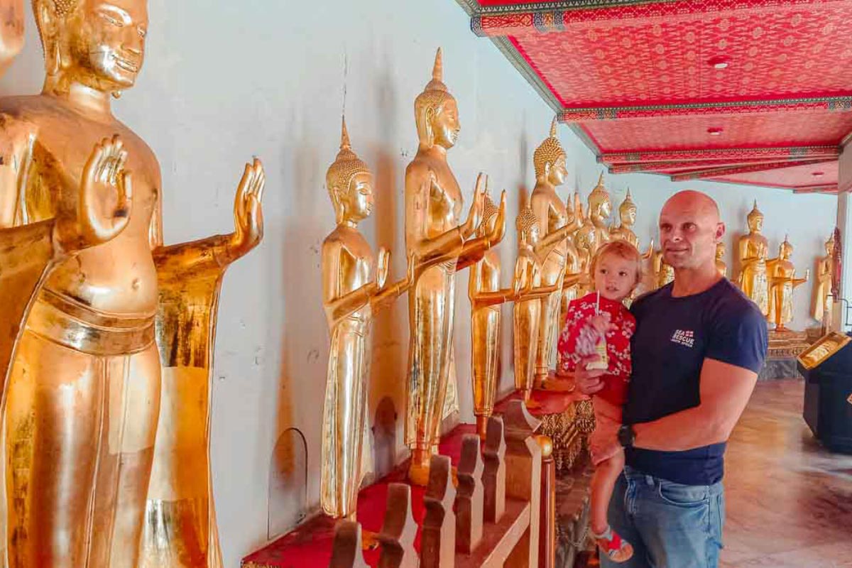 man and young daughter looking at golden buddha statues