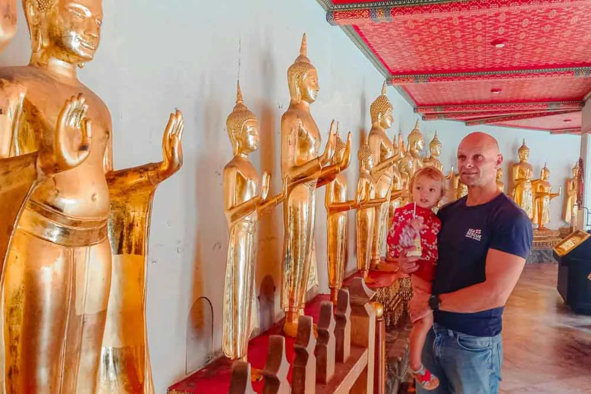 man and young daughter looking at golden buddha statues