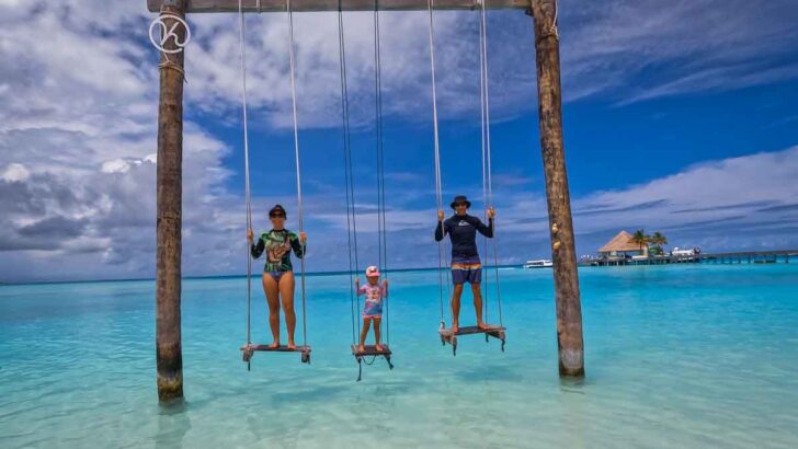 man, woman, child on swing over water, crystal clear turquiose water