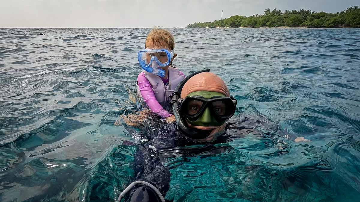 man snorkeling in clear water with child on this back