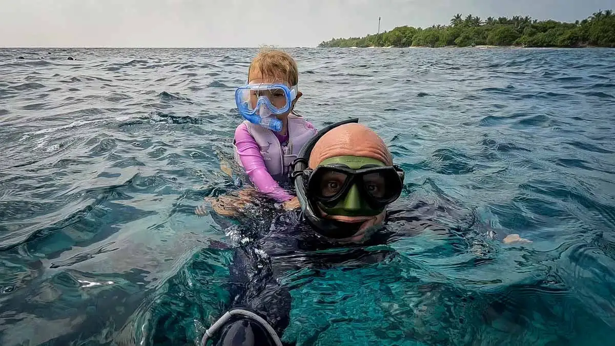 man snorkeling in clear water with child on this back