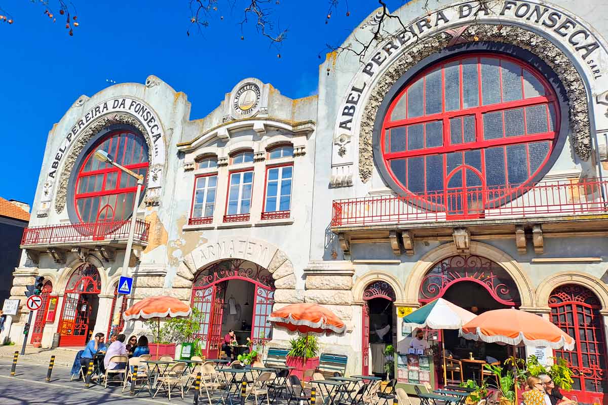 A beautiful Art-Nouveau building with big round red windows and a cafe outside