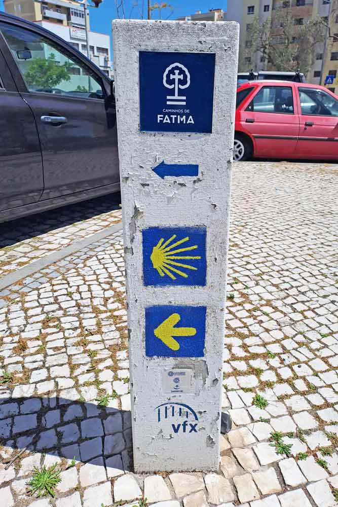 A route marker with a yellow and a blue arrow for the Camino de Santiago and Camino Fatima