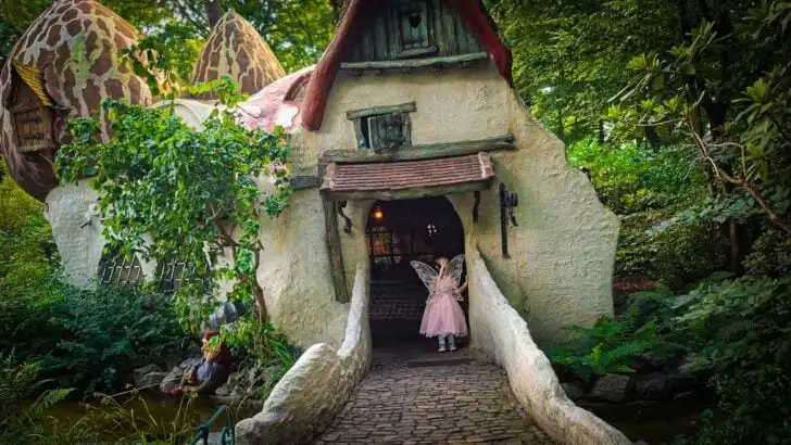 girl dressed like a pink fairy walking into fantasy house in the woods
