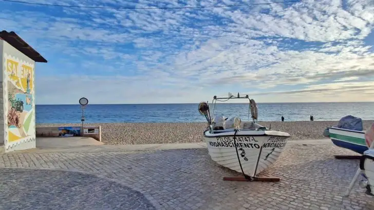 boat lying on the sidewalk, quiet beach and the ocean in the background