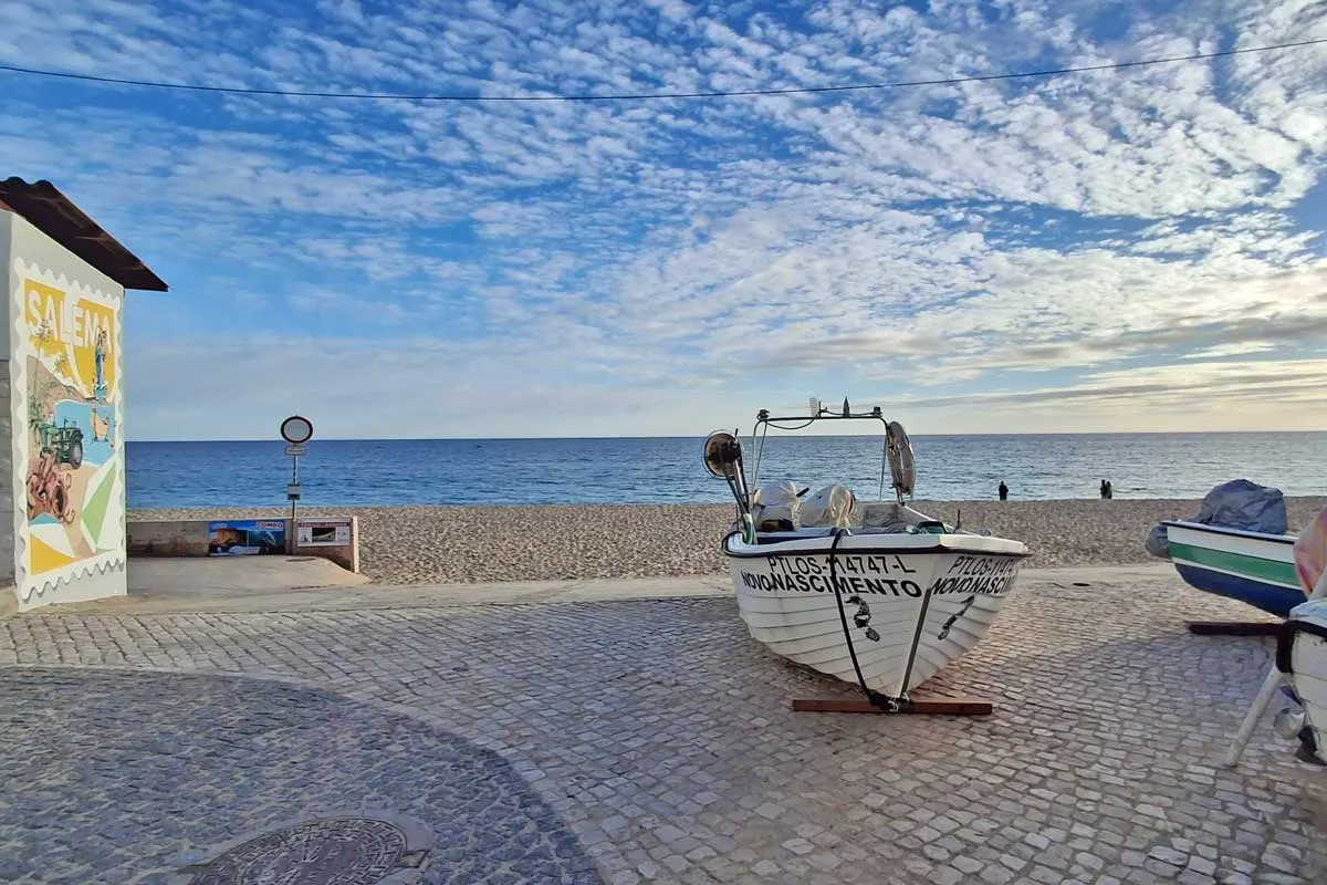 boat lying on the sidewalk, quiet beach and the ocean in the background