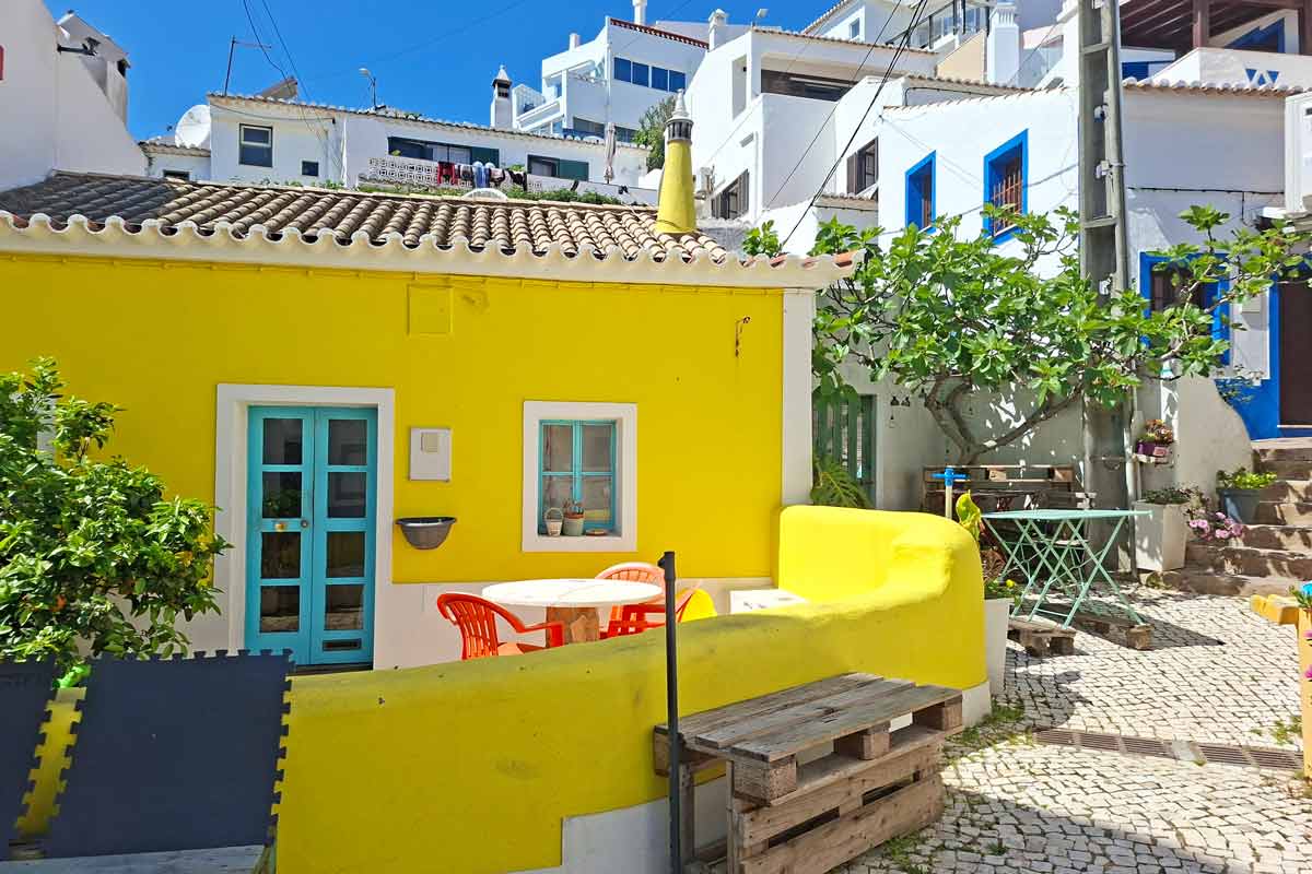 A small bright yellow house with a blue door and window near the beach in Burgau
