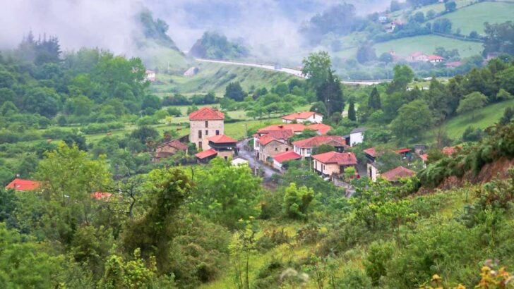 A ground of stone houses with red roofs surrounded by the lush green hills in Asturias, Spain