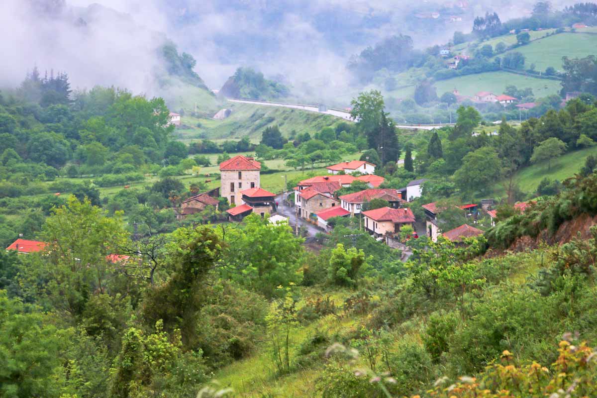 A ground of stone houses with red roofs surrounded by the lush green hills in Asturias, Spain
