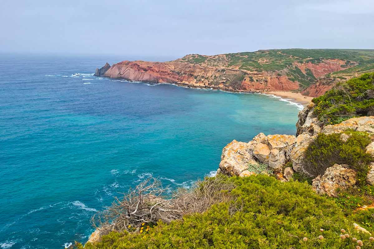 Turquoise color water, rocky cliffs, and a sandy beach on the trail from Cabo de Sao Vicente