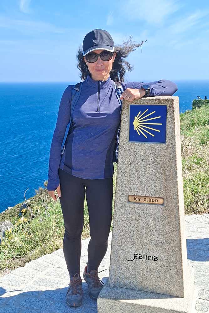 Alya next to KM0 Camino sign at Cape Finisterre