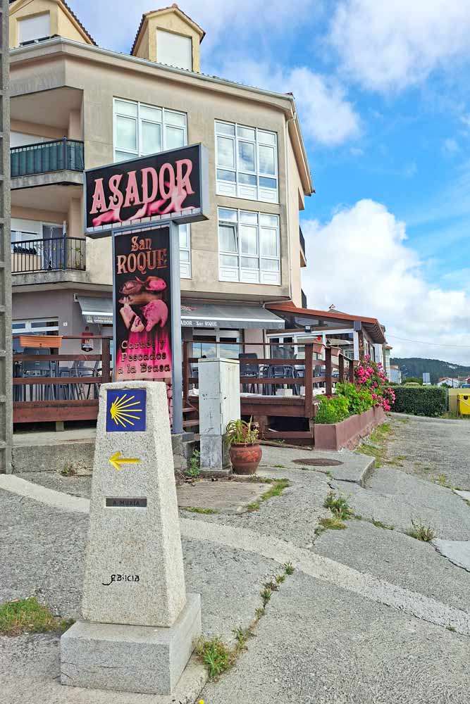 A traditional Camino sign  indicating a route in front of a grill restaurant in Finisterre
