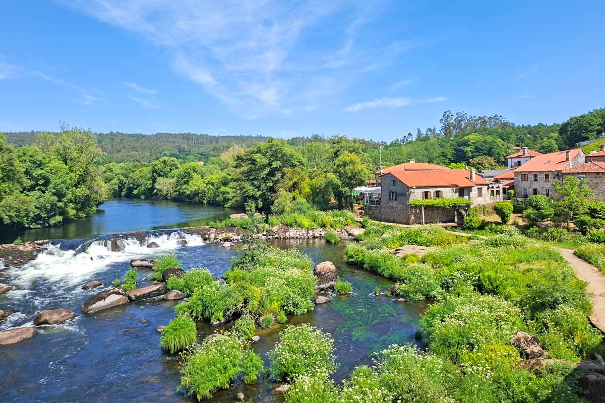 A couple of houses next to the river with small waterrfalls surrounded by the forest in Galicia