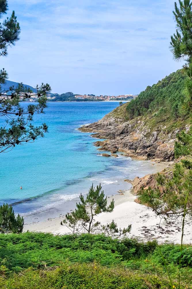 A small white-sand beach surrounded by the cliffs and forest near Finisterre, Spain