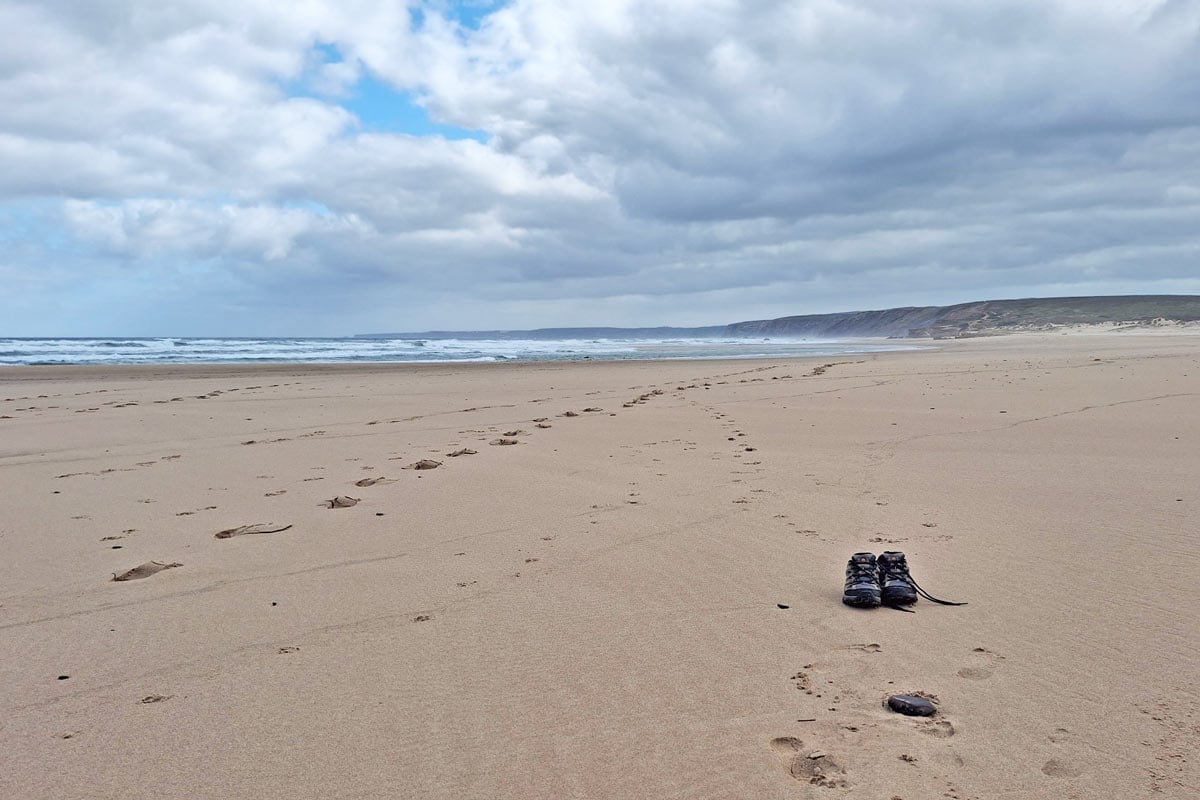 very large beach with pair of hiking shoes standing on the beach